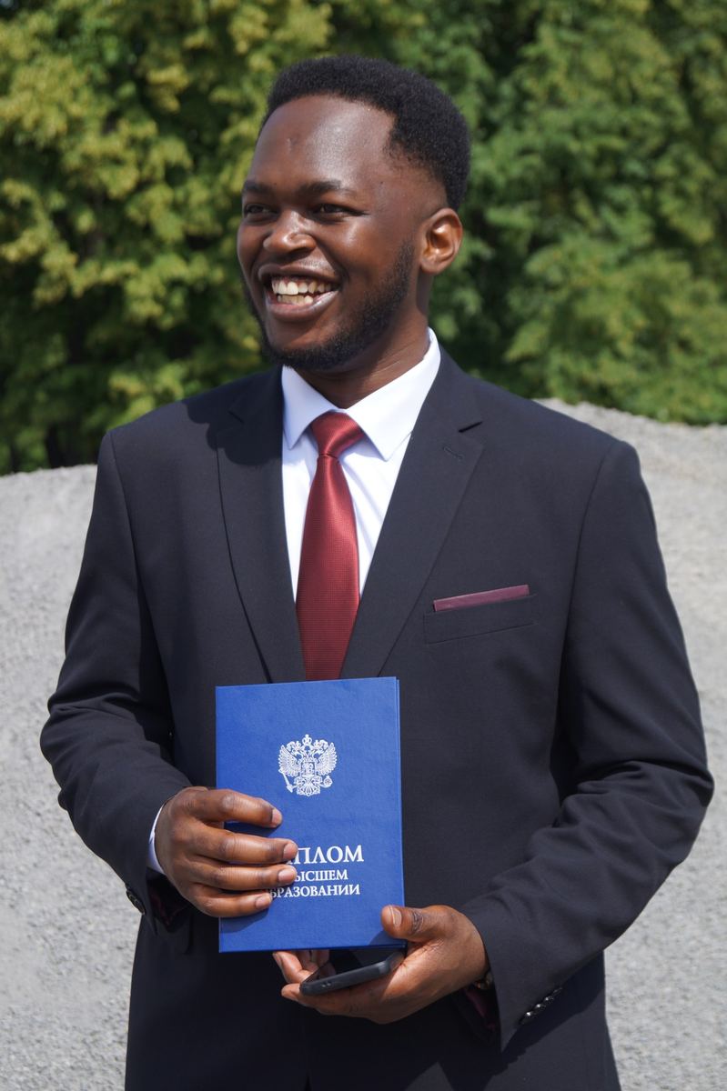 Tafadzwa in a suit holding his bachelor's diploma