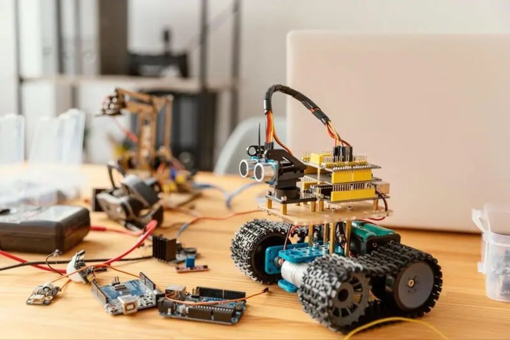 A small tracked RC rover built from stacked microcontroller boards on a workbench